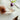A lit tealight candle inside a bird shape white ceramic round holder on a white table next to a flower.
